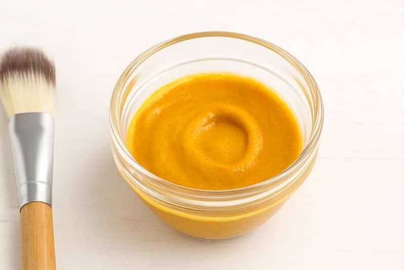DIY turmeric under eye mask in small bowl with brush and turmeric powder
