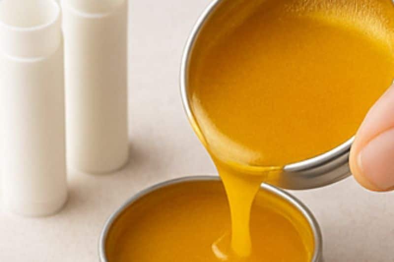 Pouring warm turmeric lip balm into small tins and tubes to set